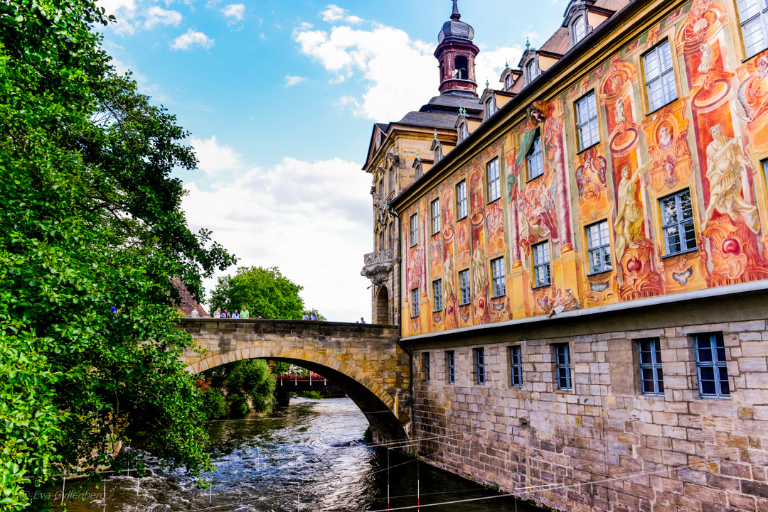 Det dekorerade rådhuset i Bamberg med bilder i rött, gult och orange, omgivet av vatten.