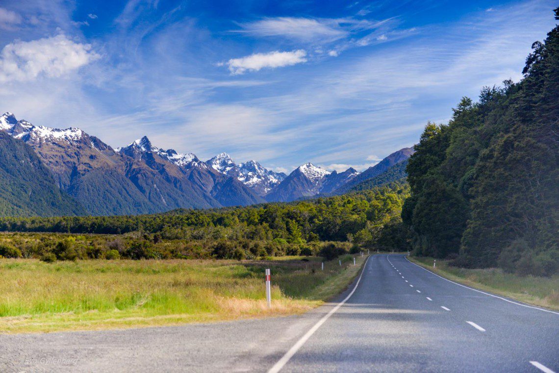 Straight road by snow-capped mountains on the way to Milford Sound