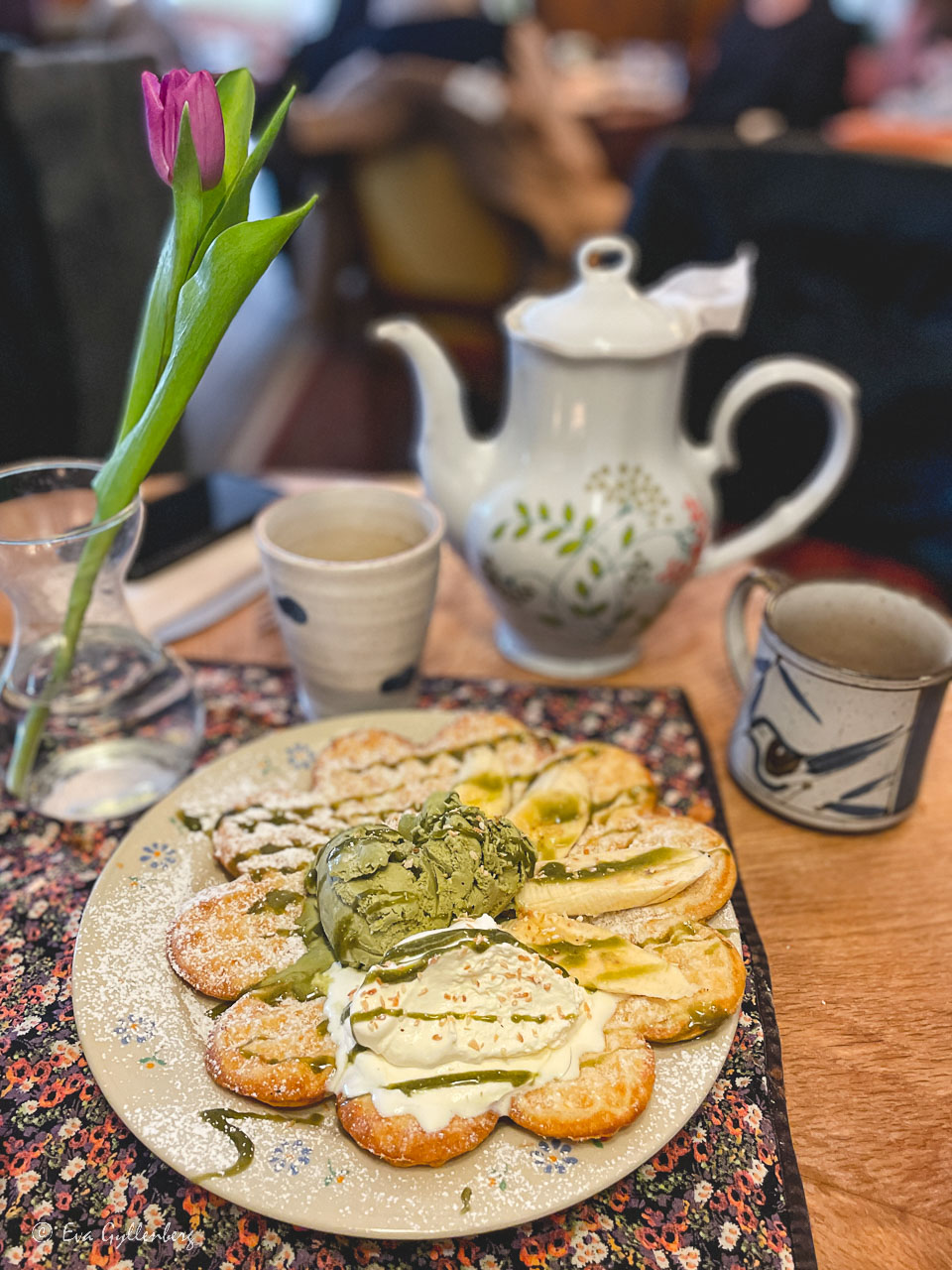 Våffla med machaglass på ett bord med en kanna kaffe och en tulpan