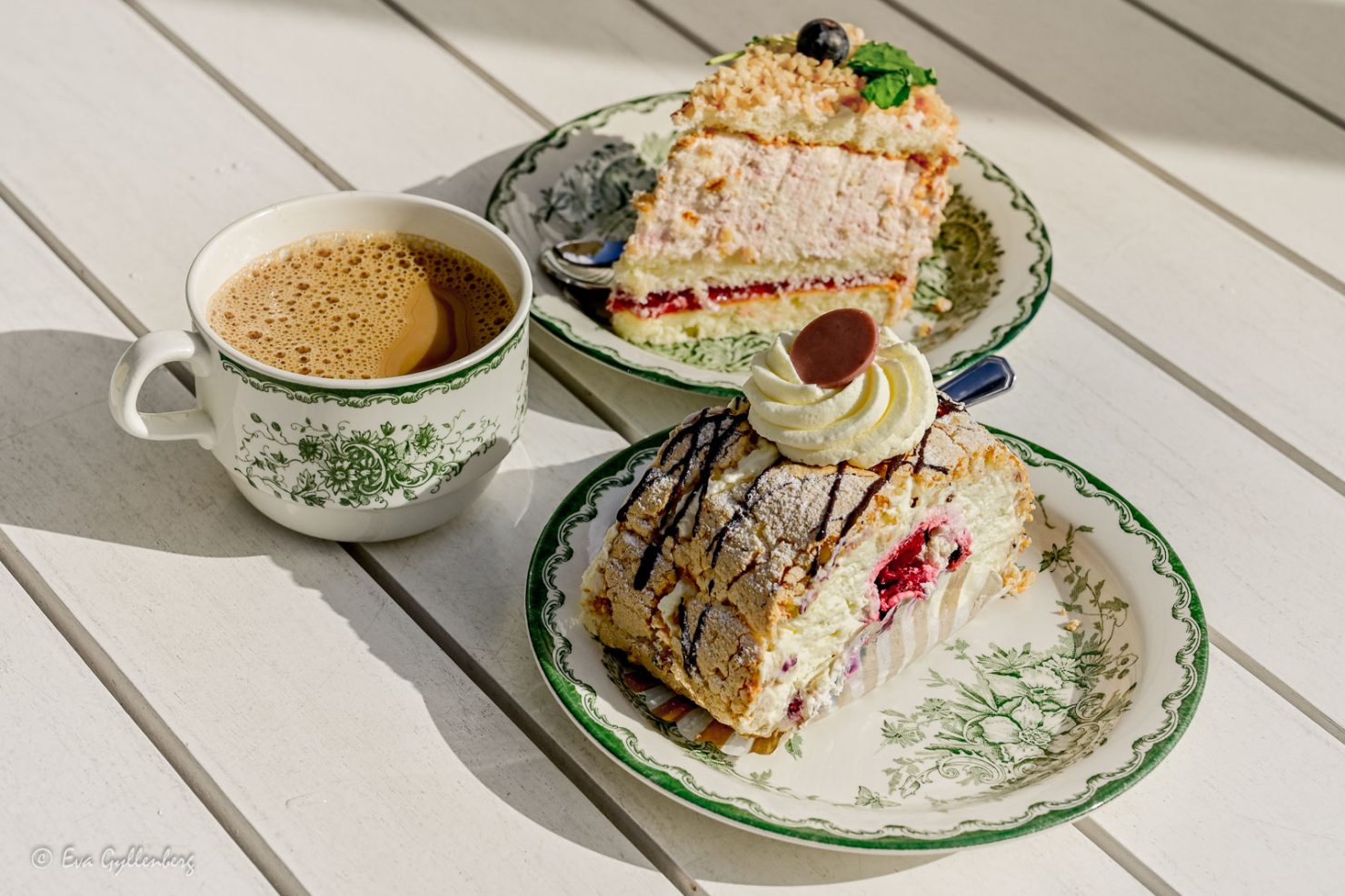 två tårtor på gröna anna-fat och en kaffekopp på ett vitt bord - en härlig fika i Åhus