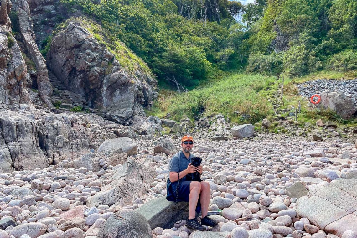 Man och hund sitter på stranden i Josefinelust i Kullaberg