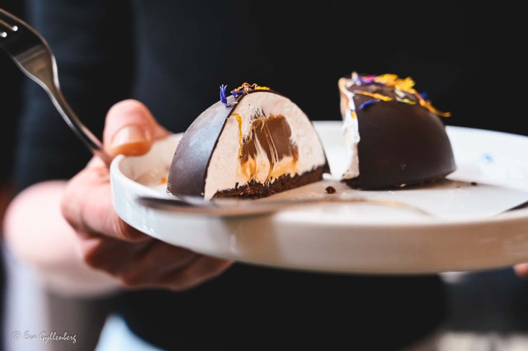 en bakelse med choklad, vitt fluff och kola på en tallrik som hålls av en hand