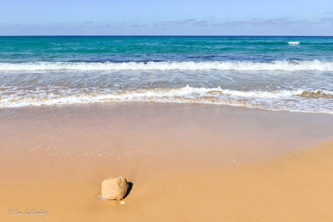 en sten på en gyllene havsstrand med turkost vatten