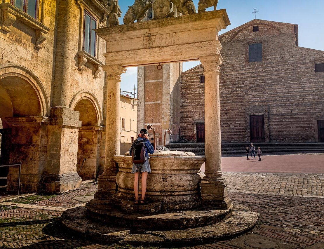 Girl looks down into well in the square of Montepulciano