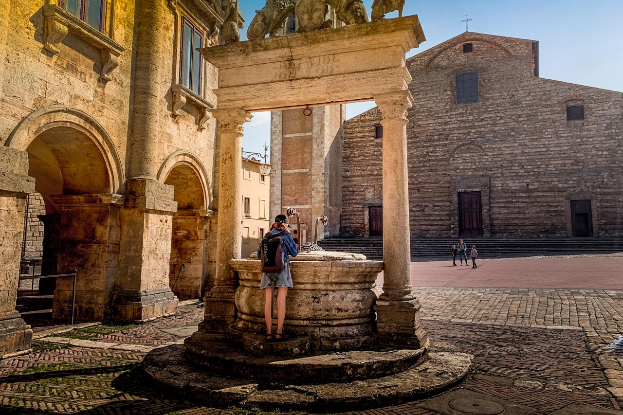 Flicka tittar ner i brunn på torget i Montepulciano