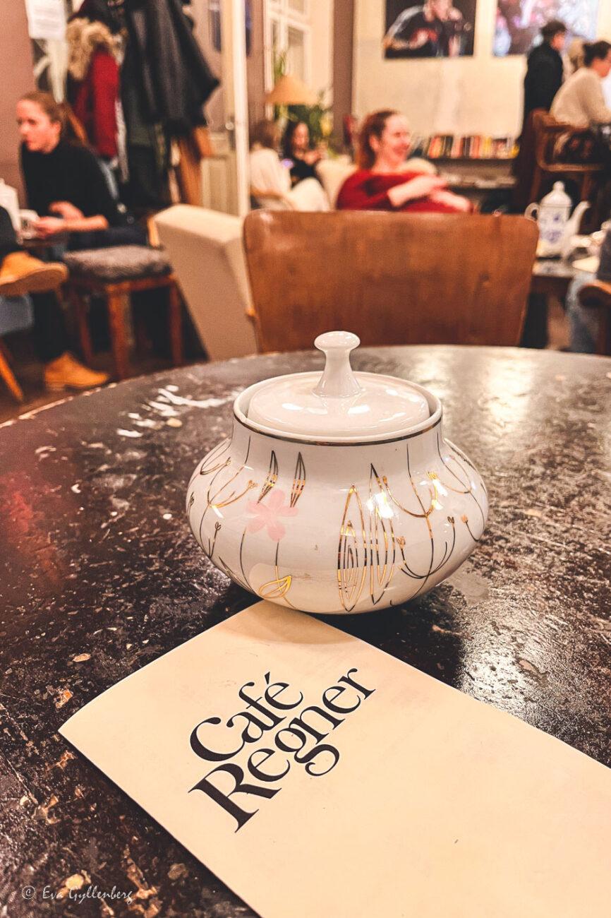 A sugar bowl on a table with people in the background