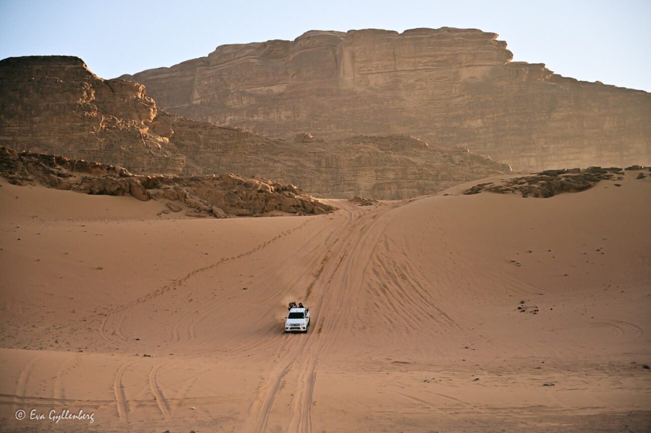 White car goes down a steep sand dune in the desert