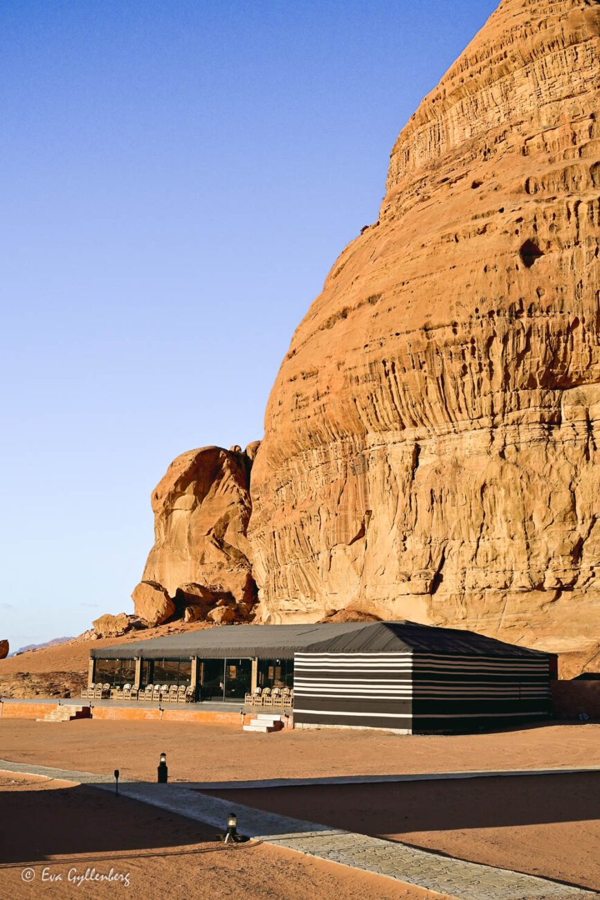 Black building in the desert under a steep cliff