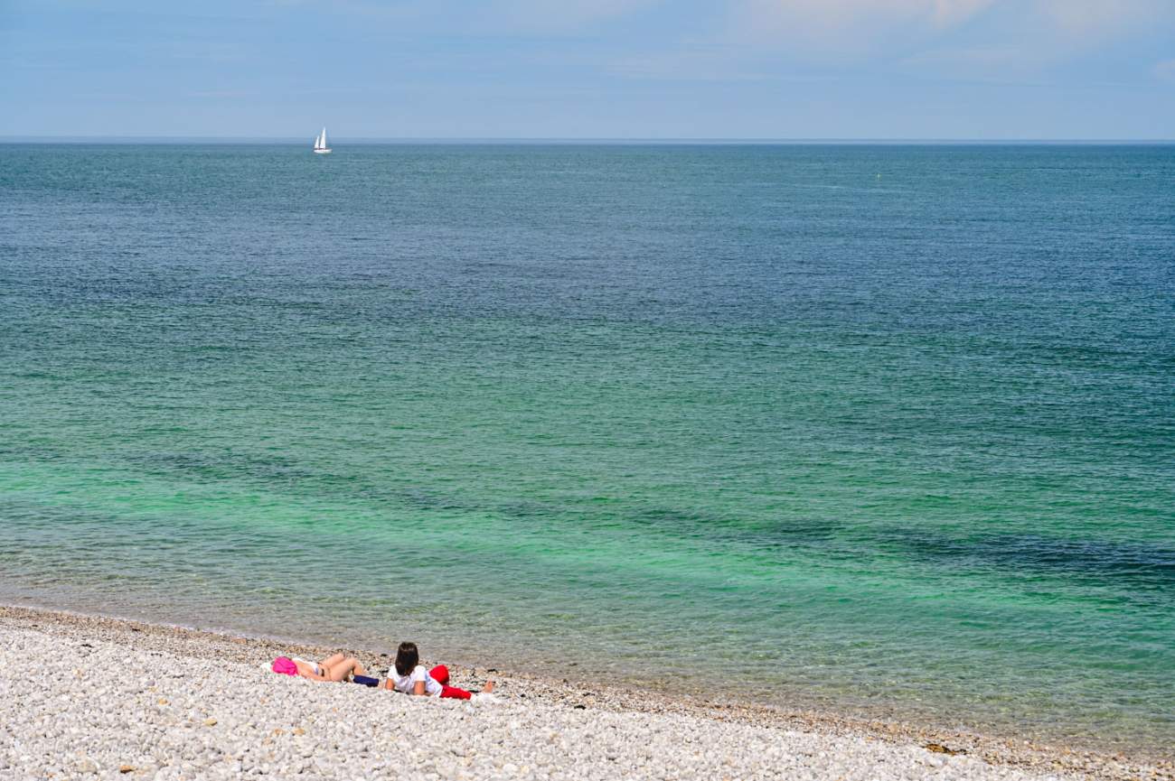 två människor ligger på en vit strand och blickar ut över ett turkost hav