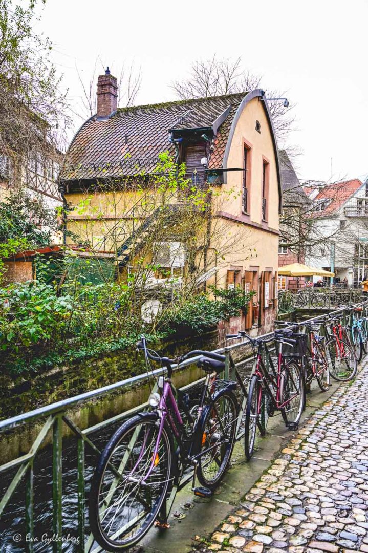 Cyklar parkerade vid ett staket vid en kanal med ett gult hus bakm