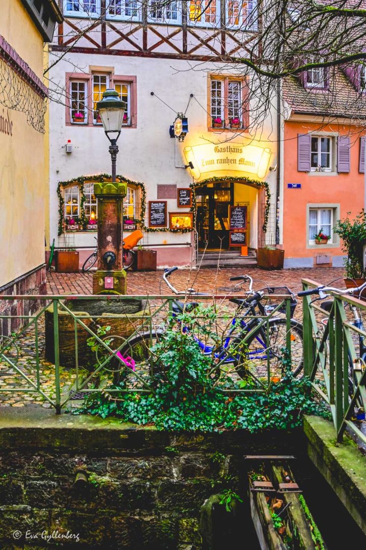 Cyklar parkerade vid ett staket vid en kanal med en restaurang i bakgrunden