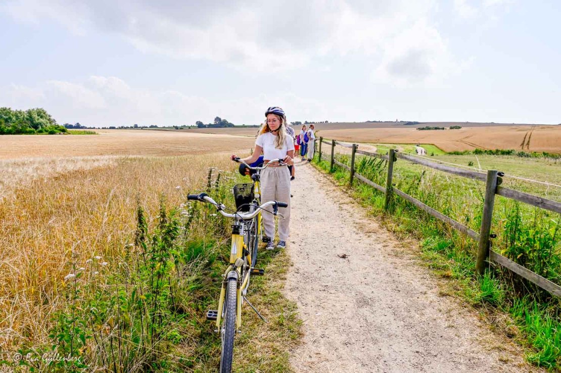 Tjej står med sin cykel på en grusväg omgiven av sädesfält